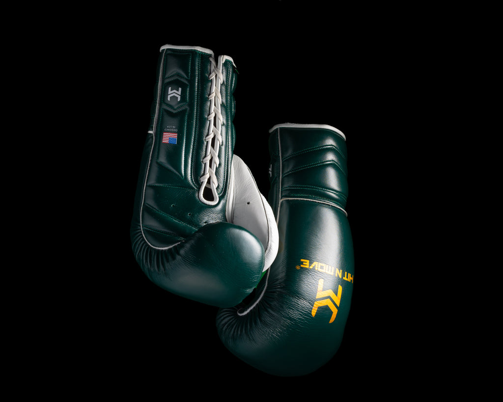 Dark green and white HIT'N'MOVE VECTOR boxing gloves with gold logos hanging by white laces against a black background