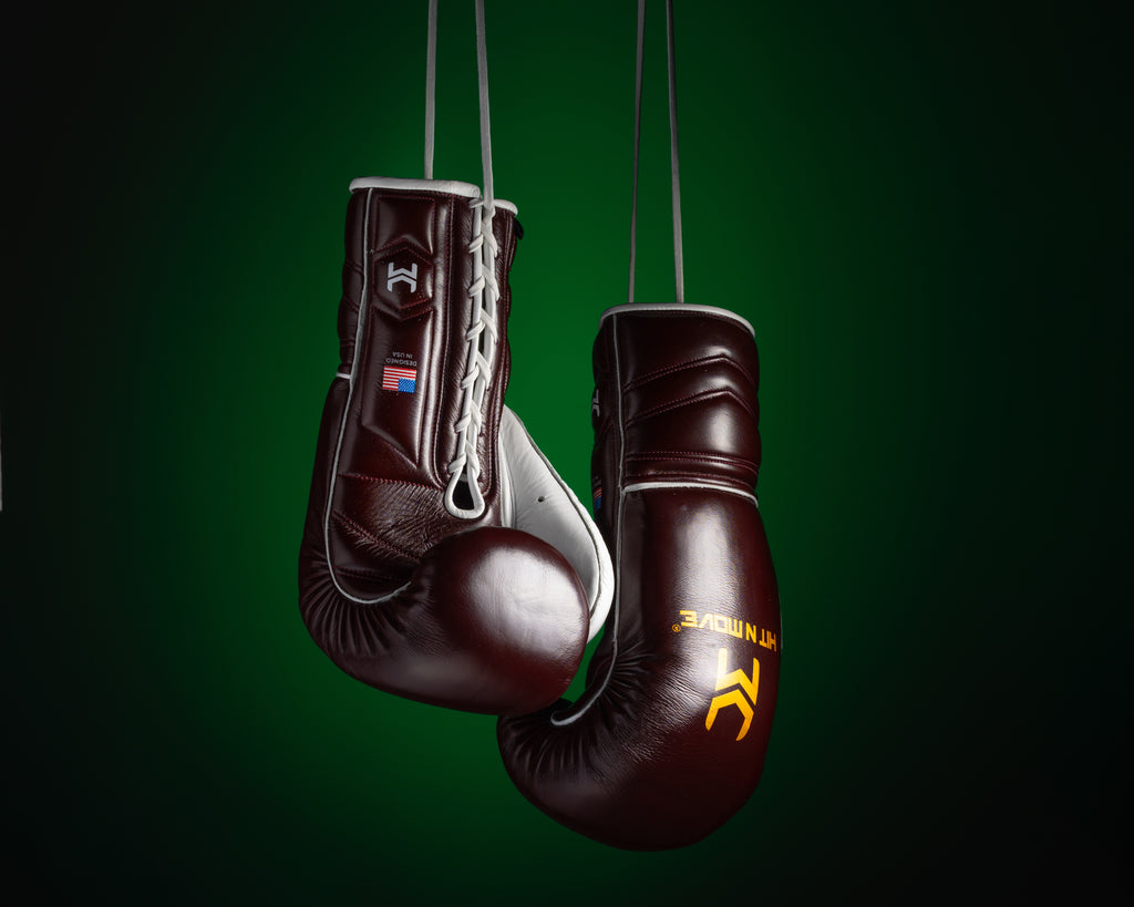 Burgundy and white HIT'N'MOVE VECTOR boxing gloves hanging by their laces against a dark green background