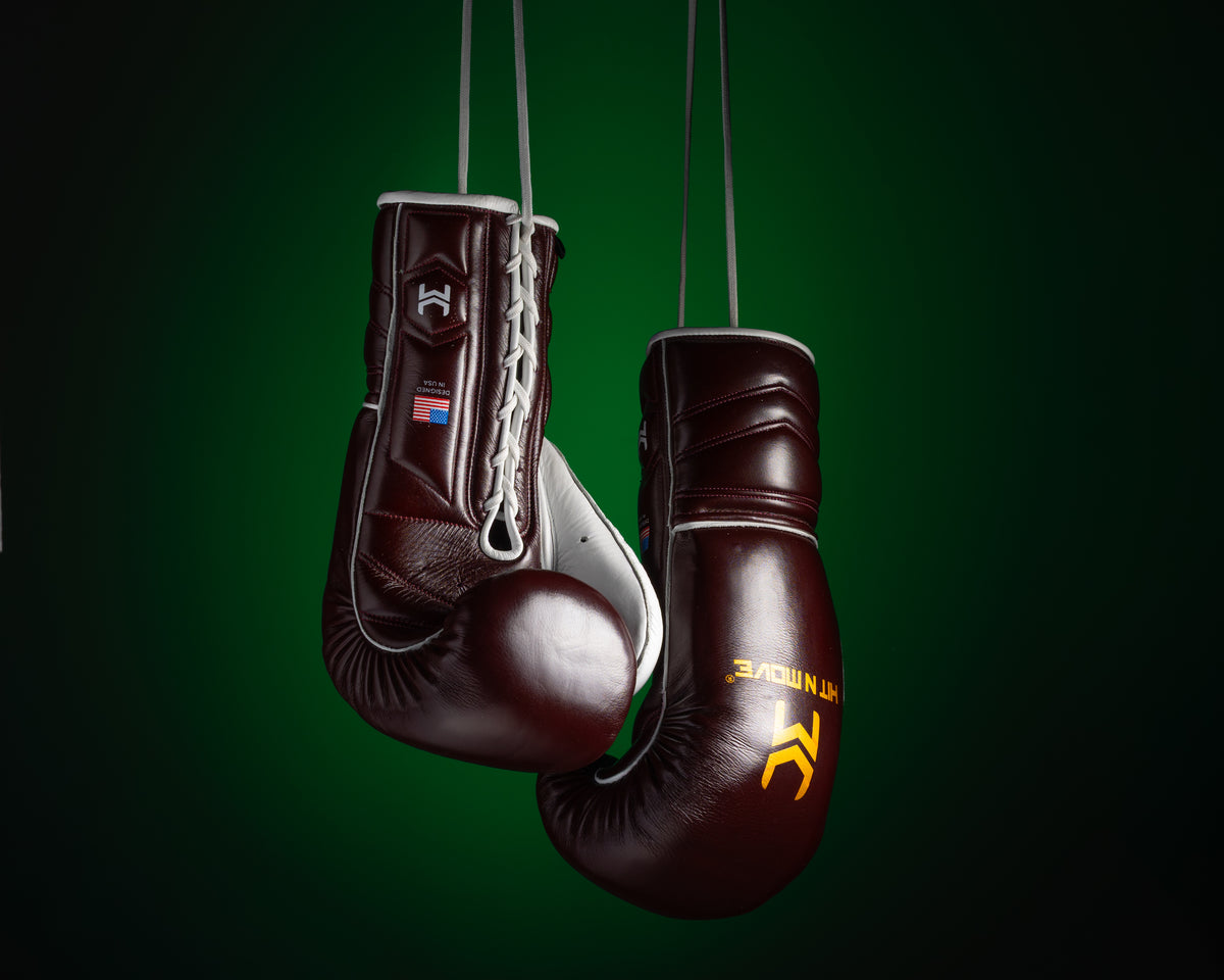 Burgundy and white HIT'N'MOVE VECTOR boxing gloves hanging by their laces against a dark green background
