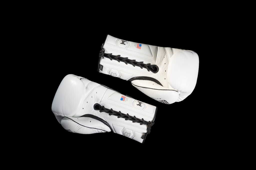 White HIT'N'MOVE VECTOR boxing gloves on a black background, showing black laces, palm sides and thumb padding